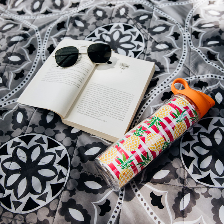 Water bottle resting on fabric alongside a book and sunglasses, creating a relaxing and leisurely scene.